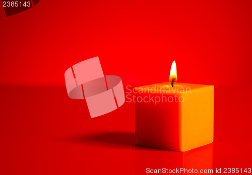 Image of Burning yellow candle over red background