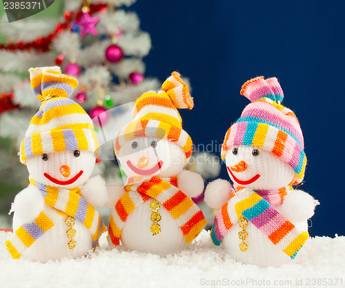 Image of Three snowmen in front of the decorated white evergreen tree ove