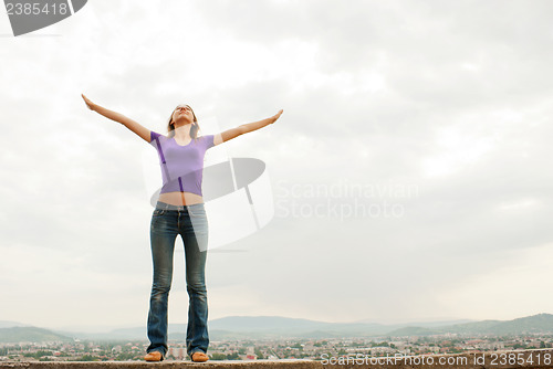 Image of Young woman staying with raised hands against blue sky