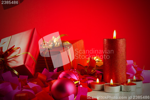 Image of Christmas gifts and candles over red background
