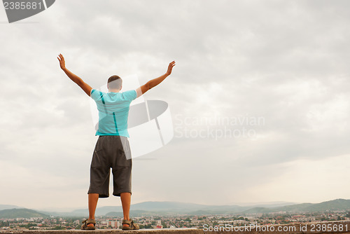 Image of Young man staying with raised hands against blue sky