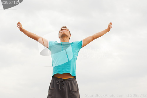 Image of Young man staying with raised hands against blue sky