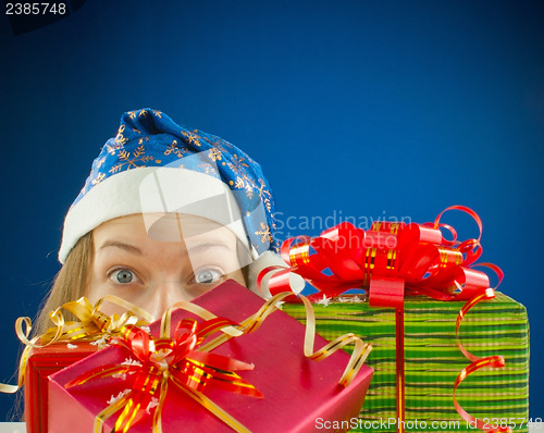 Image of Surprised teen girl looking from behind the Christmas presents