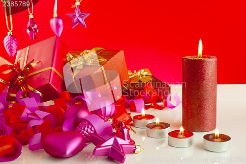 Image of Christmas gifts with candles over red background