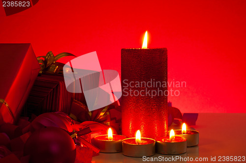 Image of Christmas gifts and candles over red background