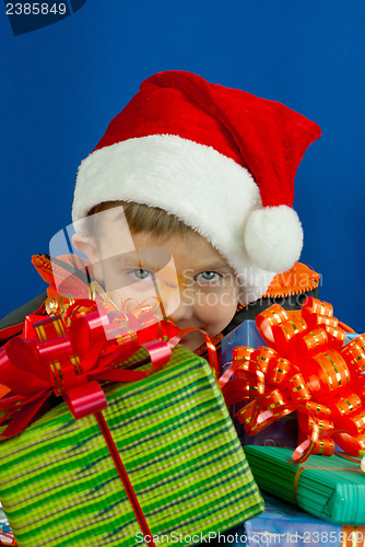 Image of Surprised boy looking from behind the Christmas presents