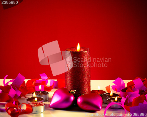 Image of Burning candles with two heart shaped toys against red background