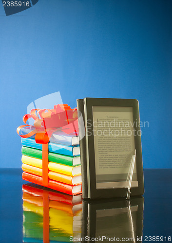 Image of Stack of books with electronic book reader against blue background
