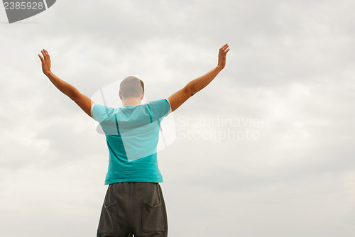 Image of Young man staying with raised hands against blue sky