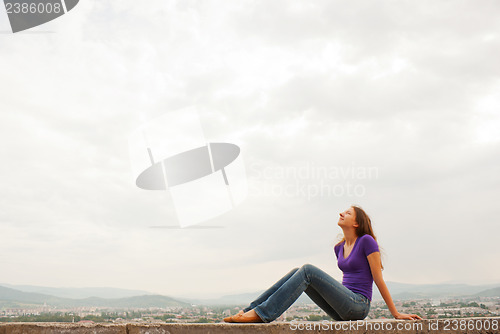 Image of Young woman sitting outdoors against blue sky