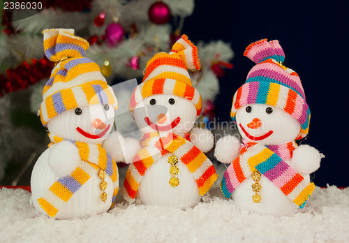 Image of Three snowmen in front of the decorated white evergreen tree ove
