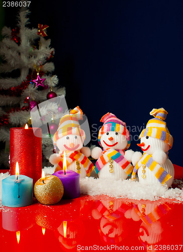 Image of Three snowmen and burning candles over the blue background