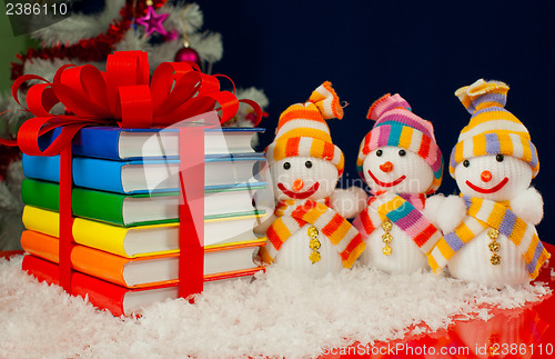 Image of Stack of colorful books tied up with red ribbon and three snowme