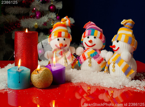 Image of Three snowmen and burning candles over the blue background