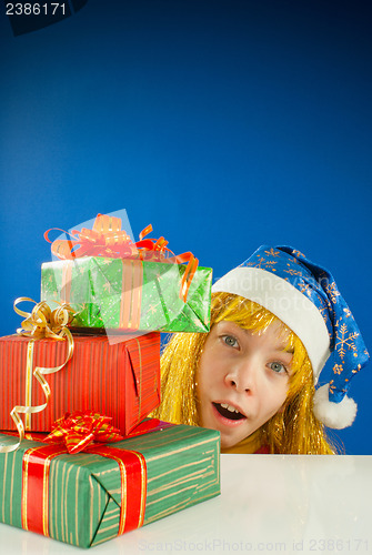 Image of Surprised teen girl looking from behind the Christmas presents