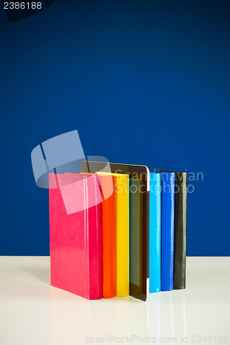 Image of Row of colorful books and tablet PC over blue background