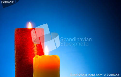 Image of Two burning colourful candles against blue background