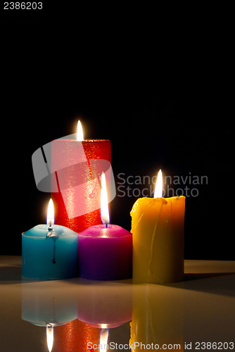Image of Four colourful burning candles against black background