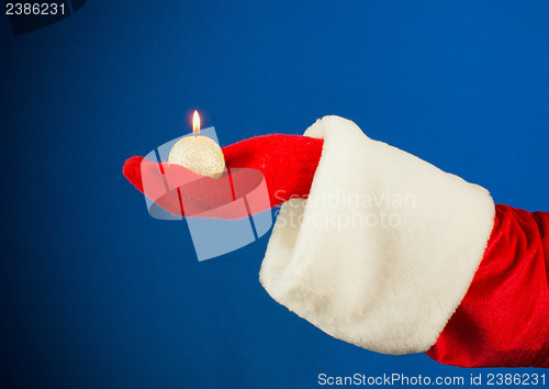 Image of Santa's hand holding a burning candle over blue background