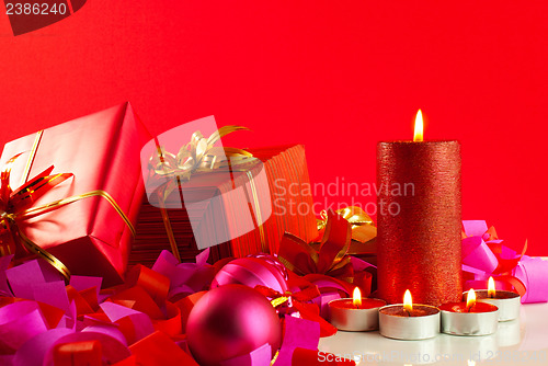 Image of Christmas gifts and candles over red background