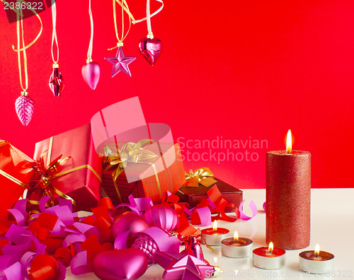 Image of Christmas gifts and candles over red background