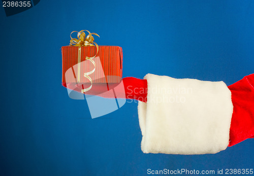Image of Santa's hand holding a present over blue background