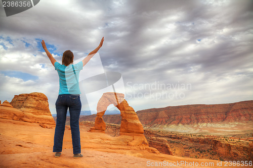 Image of Woman with raised hands in front of Delicate Arch
