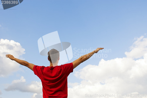 Image of Young man staying with raised hands against blue sky