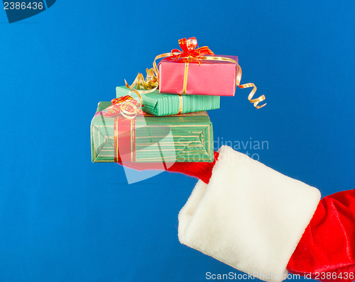 Image of Santa's hand holding presents over blue background