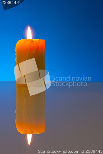 Image of Burning yellow candle against blue background