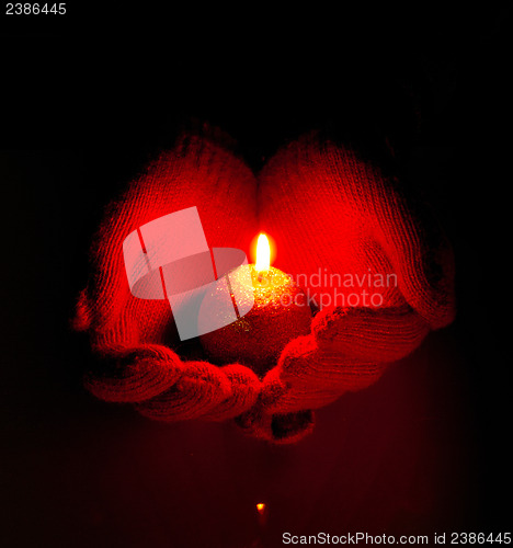 Image of Human hands hold burning candle against dark background