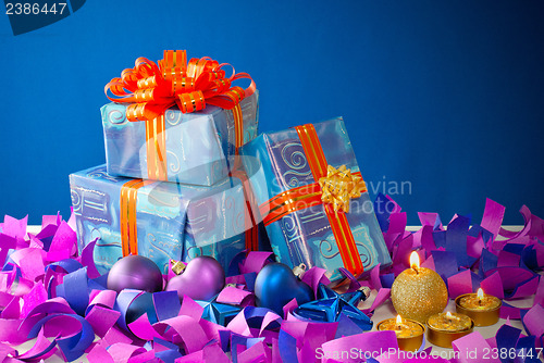 Image of Christmas gifts and candles over blue background