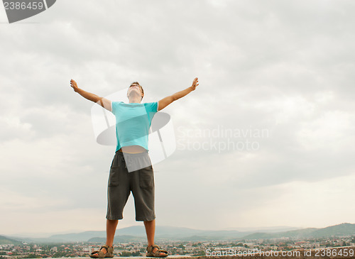 Image of Young man staying with raised hands against blue sky