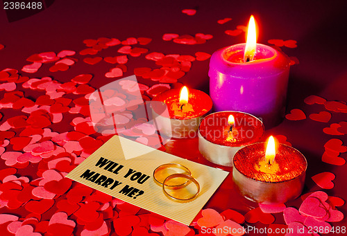 Image of Two rings and a card with marriage proposal with four candles