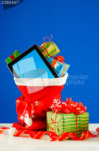 Image of Tablet PC with heap of presents in red bag against blue backgrou