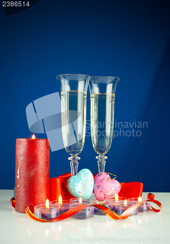 Image of Two wineglasses and burning candles against blue background