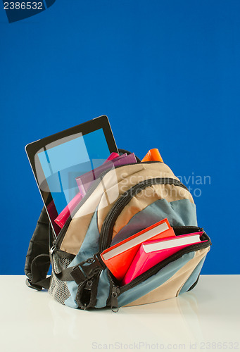 Image of Backpack with colorful books and pablet PC on the blue backgroun