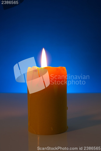 Image of Burning yellow candle against blue background