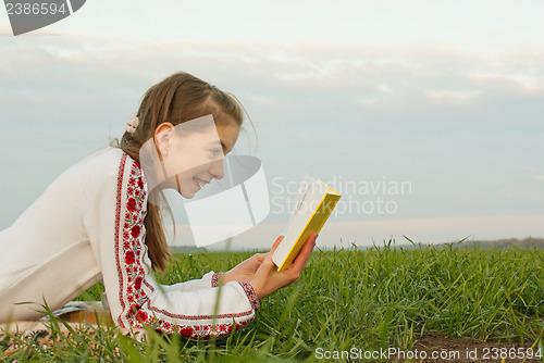 Image of Teen girl reading a book at a field