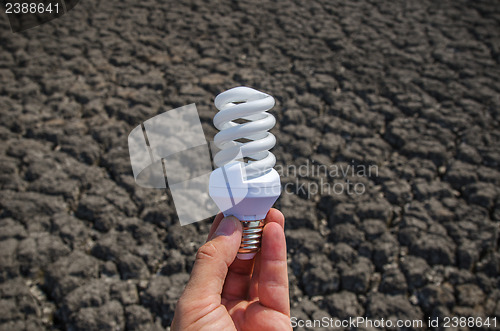 Image of energy saving lamp in hand over drought earth