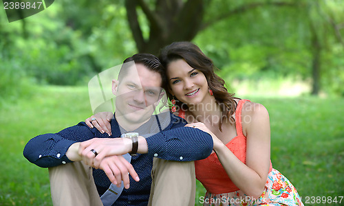 Image of Happy young couple posing seated on the ground in a garden setti