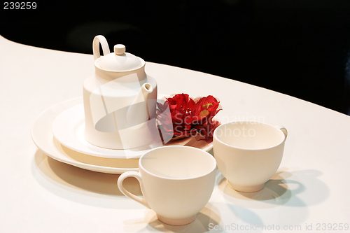 Image of White teapot, cups and saucers with a red flower