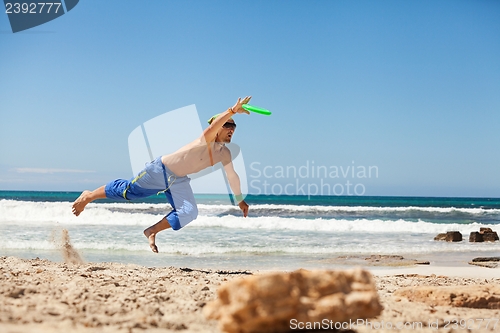 Image of attractive man playing frisby on beach in summer