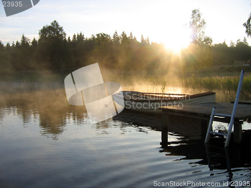 Image of Small boat in a misty lake at sunrise.