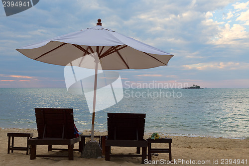 Image of Two beds and an umbrella on the beach at sunset