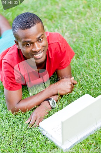 Image of young smiling african student sitting in grass with notebook