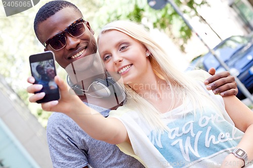 Image of young smiling multiracial couple taking foto by smartphone 