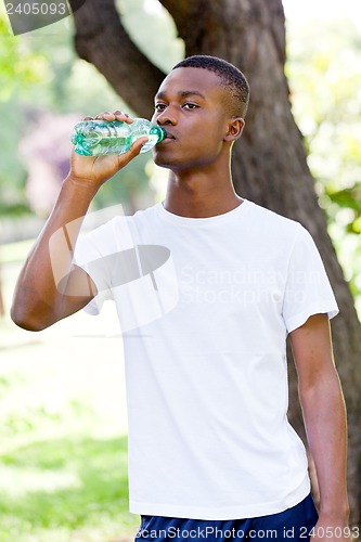 Image of athletic african young man drinking water outdoor