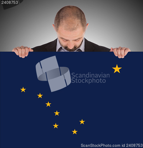 Image of Smiling businessman holding a big card, flag of Alaska