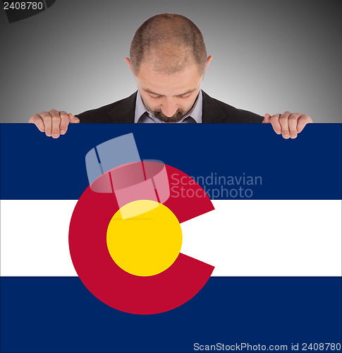 Image of Smiling businessman holding a big card, flag of Colorado